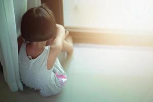 una niña triste estaba llorando y sentada en el suelo cerca de la puerta de la habitación. ella fue intimidada, infeliz, molesta, se siente enferma. concepto solitario. foto