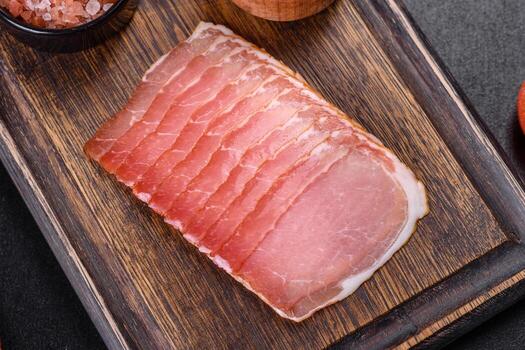 Smoked ham on a dark concrete table with addition of fresh aromatic herbs and spices photo