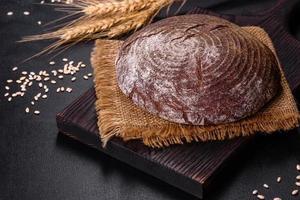 Fresh baked homemade brown bread on a black concrete background with wheat grains