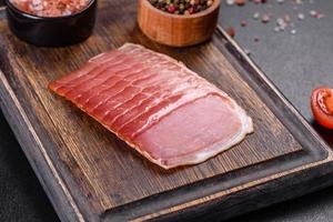 Smoked ham on a dark concrete table with addition of fresh aromatic herbs and spices photo