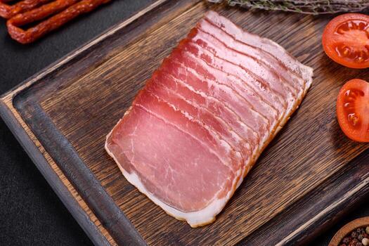 Smoked ham on a dark concrete table with addition of fresh aromatic herbs and spices photo