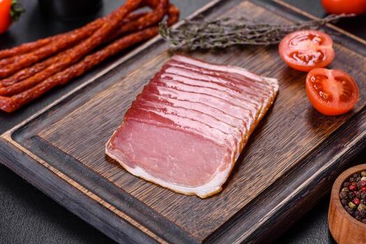 Smoked ham on a dark concrete table with addition of fresh aromatic herbs and spices photo
