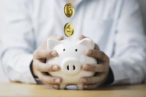 Businessman holding white piggy bank saving with golden coins falling for deposit and money saving investment concept. photo