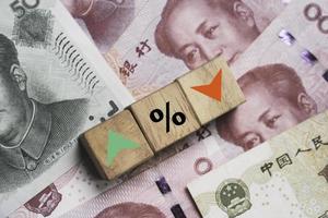 Increasing and decreasing sign with percentage on wooden cube block and Yuan banknotes for forex currency exchange money transfer rate concept. photo