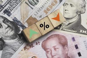 pantalla de impresión de porcentaje creciente y decreciente a bloque de cubo de madera en billetes de dólar usd y yuan por concepto de tipo de cambio de moneda. foto
