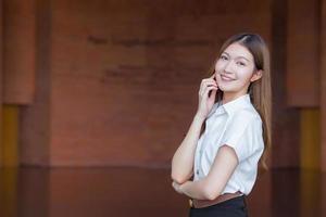 retrato de un estudiante tailandés adulto con uniforme de estudiante universitario. hermosa chica asiática de pie con los brazos cruzados sobre un fondo de ladrillo.