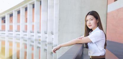 retrato de un estudiante tailandés adulto con uniforme de estudiante universitario. hermosa chica asiática sentada sonriendo felizmente en la universidad foto