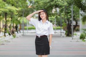 Young Asian woman student who has blond long hair smiles and looks at to camera while standing in university with outdoor garden tree background. photo