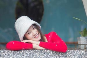 retrata la hermosa piel de una mujer asiática que usa un cárdigan rojo de manga larga y un sombrero de crema sonríe alegremente y mira la cámara.