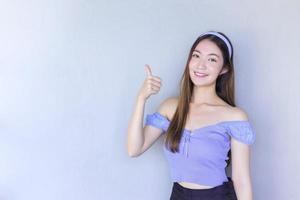 Young beautiful Asian woman is acting thumb up as a good symbol and another hand shows as presenting something on the background. photo