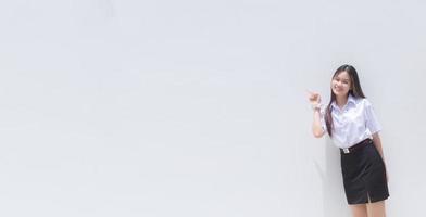 A beautiful Asian girl in a cheerful school uniform is smiling and showing her finger to present some product with a white background. photo