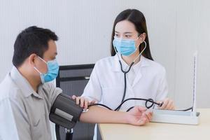 Asian woman doctor uses stethoscope and a blood pressure motoring to measure blood pressure of the man patient. In healthcare concept,