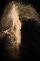 Abstract river sand cloud. Golden colored sand splash against black background. Yellow sand fly wave in the air. photo