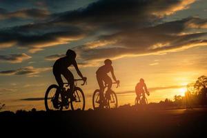 The men ride  bikes at sunset with orange-blue sky background. Abstract Silhouette background concept. photo