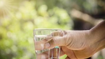 Young man holds glass with pure water on light background. Concept of health, thirst, heat and beauty care. photo