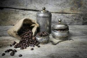 taza de plata y granos de café en bolsa de tela de saco sobre fondo de madera foto