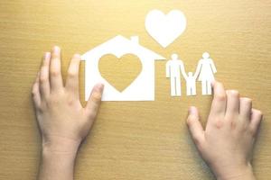children hands with small model of house and heart and family on wooden background photo