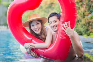 Cheerful young friends having fun in heart shaped inflatable, Happy young couple having fun at swimming pool. Happiness lifestyle concepts photo