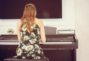vista trasera de una mujer hermosa vestida tocando el piano, una joven tocando el piano de cola en casa foto