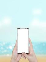 Woman's hand holding smartphone with blur sea natural background. photo