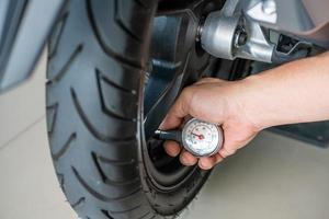 Hand holding portable tire pressure gauge checking air pressure for  motorcycle tire.  maintenance, repair motorcycle concept in garage .selective focus photo