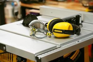 Earmuffs and Safety glasses on Electric saw table in workshop .Work safety concept . selective focus photo