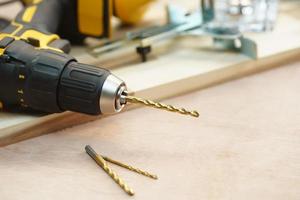 poco de eneldo Taladro eléctrico o destornillador inalámbrico en madera contrachapada de nogal en taller, artesanía en madera y concepto de bricolaje. enfoque selectivo foto