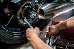 mecánico que usa una llave y un zócalo en la rueda dentada de la motocicleta. concepto de mantenimiento y reparación en el garaje de motocicletas. enfoque selectivo foto