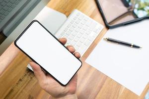 hand holding smartphone with blank screen near working desk,Social media ,communication,technology device concept photo