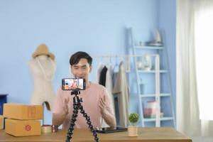 An Asian man is showing clothes in front of smartphone  live streaming at his shop. Technology online business concept. photo