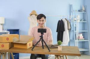 An Asian man is showing clothes in front of smartphone  live streaming at his shop. Technology online business concept. photo