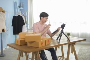 An Asian man is showing clothes in front of smartphone  live streaming at his shop. Technology online business concept. photo