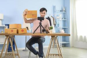 An Asian man is showing clothes in front of smartphone  live streaming at his shop. Technology online business concept. photo