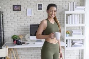 mujer joven fitness en ropa deportiva tomando una taza de café después de hacer ejercicio en casa, saludable y estilos de vida. foto