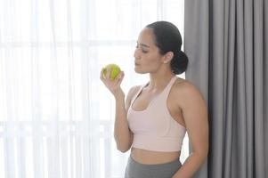 Fit young woman eating an apple after work out at home, sport and healthy lifestyle concept. photo