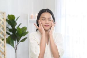 Happy beautiful woman in white bathrobe applying moisturizing cream on face , skin care and treatment concept photo