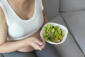 mujer joven embarazada con ensalada en casa, atención médica y atención del embarazo foto