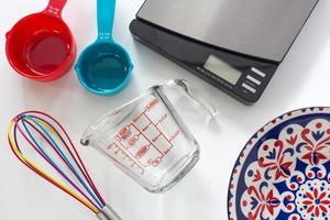 Measuring cups made from colorful plastic and glass, digital scale and whisk use in cooking lay on white background. photo