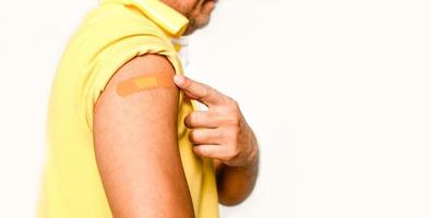 An orange plaster is attached to the man's arm. Concept for first aid after coronavirus COVID-19 vaccination, and professional, medical, needle, blood, cancer. Closeup, white blurred background