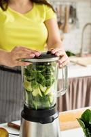 mujer joven haciendo batido de espinacas verdes en la cocina de casa foto