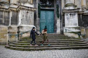 una pareja joven de moda camina por la ciudad, la joven tiene bolsas de compras en el brazo y el hombre una taza de café en la mano foto