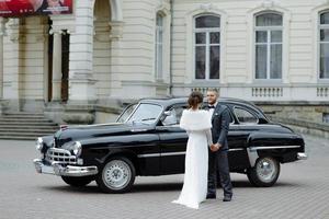 Happy luxury wedding couple kissing and embracing near retro with bouquet car in autumn photo