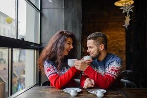 Happy and romantic couple in warm sweaters drink coffee from disposable paper cups in cafeteria. Holidays, christmas, winter, love, hot drinks, people concept photo