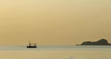 Silhouette of fishermen collecting fishing gear on a small fishing boat. The sea in the sunrise. Golden hour. photo