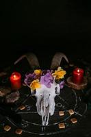 scull de cabra blanca con cuernos, flores, libro viejo abierto, velas en la mesa de brujas. foto