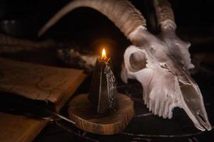 scull de cabra blanca con cuernos, libro antiguo abierto, hechizos mágicos, runas, velas negras foto