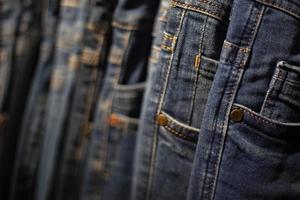 primer plano muchos jeans colgando de un estante. fila de pantalones vaqueros colgados en el armario. foto