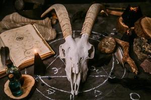 scull de cabra blanca con cuernos, libro antiguo abierto, hechizos mágicos, runas, velas negras foto