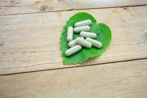 Cápsulas de hierbas medicinales con hoja de hierba verde sobre mesa de madera foto