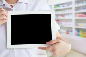 female pharmacist using tablet pc against close up of shelves of drugs photo